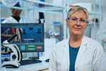 Portrait of old scientist woman smiling at camera in modern equipped lab. Multiethnic team examining virus evolution using high tech and chemistry tools for scientific research, vaccine development.